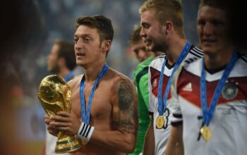 Mesut Özil yang bertelanjang dada memegang trofi Piala Dunia 2014 sambil mengenakan medali emas di lehernya, sebuah momen puncak dalam kisah Mesut Özil.